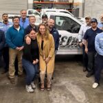 A group of people pose together in a warehouse in Southern California, some in uniforms and others in casual or business attire, standing before a white van labeled "Elite Pest Management, Inc.," now part of the CERTUS Pest acquisition.