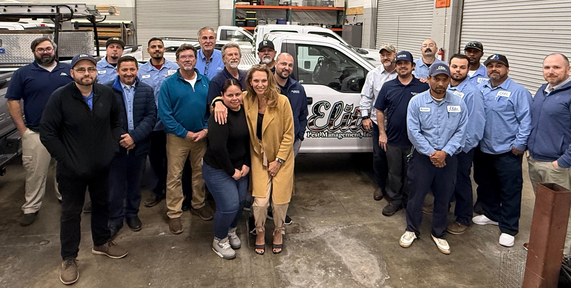 A group of people pose together in a warehouse in Southern California, some in uniforms and others in casual or business attire, standing before a white van labeled "Elite Pest Management, Inc.," now part of the CERTUS Pest acquisition.